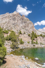 The beautiful mountain trekking road with clear blue sky and rocky hills and the view of Alaudin lake in Fann mountains in Tajikistan