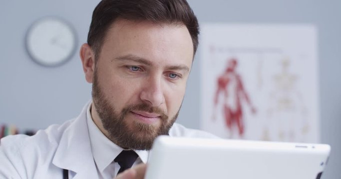 Close-up portrait of doctor with statoscope writting prescription for medication, texting patients using tablet. Therapist consulting online during quarantine. Сoncept of pandemic, modern medicine.