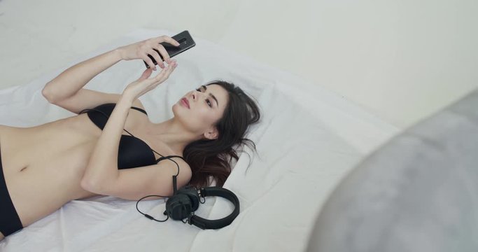 Top view of happy girl in black lingerie lying on bed and using smartphone