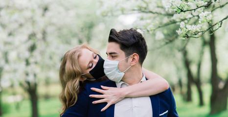 Young loving couple walking in medical masks in the park during quarantine on their wedding day. Coronavirus, disease, protection, sick, illness flu europe celebration canceled.