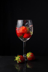 Close-up of glass cup with strawberries, two strawberries, on slate with reflection, black background, vertical, with copy space