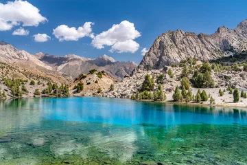 The beautiful mountain trekking road with clear blue sky and rocky hills and the view of Alaudin lake in Fann mountains in Tajikistan