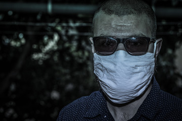 Man wearing a white cloth face mask and black sunglasses in a strange sad portrait, green teal tint in night time bizzare environment