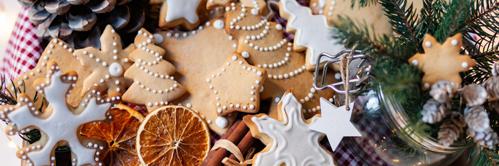 Wooden box with delicious homemade gingerbread cookies with white icing. Perfect beautiful gift in rustic style. Orange, cones, fir tree branches and lights as decor. Close up. Banner