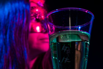 A cup of liquor and a woman in mask in a bar.