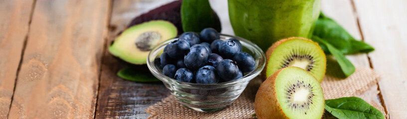 Healthy food and vegan diet concept - glass of fresh green juice or smoothie with kiwi, spinach, blueberry, avocado. Antioxidant detox beverage with raw ingredients.  Close up, wooden background.
