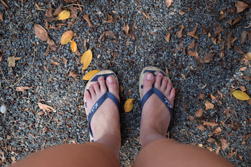 Girl&rsquo;s feet with flip-flops among pebbles and orange leaves