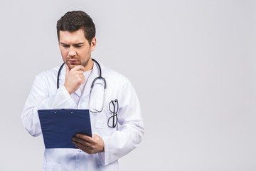 Portrait of serious male young doctor holding clipboard isolated on white background.