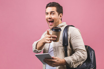 Young man with backpack holding coffee cup and tablet computer isolated on pink background. Smiling student portrait. Studio shot of cheerful men going on travel.