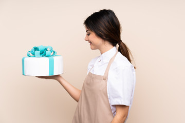 Pastry chef woman holding a big cake over isolated background with happy expression