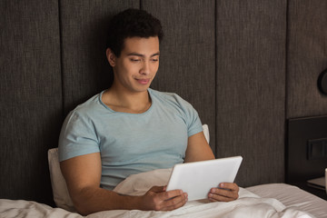 Naklejka premium handsome mixed race man using digital tablet in bed during self isolation