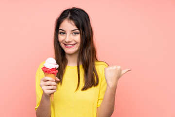 Young brunette woman holding a cornet ice cream over isolated pink background pointing to the side to present a product