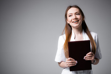 Happy redhead Irish doctor in a white coat smiles and holds a folder with medical documents on an gray background