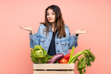 Young farmer woman holding a basket full of fresh vegetables having doubts with confuse face expression