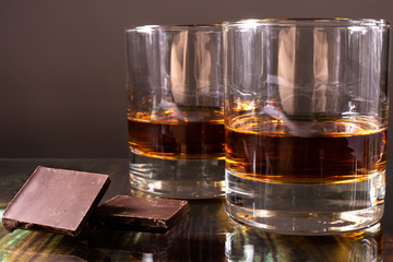 Whiskey in a glass and dark chocolate. Strong elite alcohol and snack.