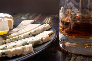 Whiskey in a glass and appetizer - blue cheese and camembert cheese. Strong elite alcohol and snack.