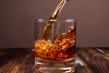 
Whiskey is poured into a glass. Fiery high-end alcoholic drink in a bar on a dark wooden background.