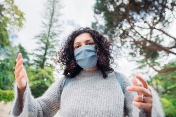 Woman in a medical mask gesticulating with her hands, complaining about the virus. Green trees on...