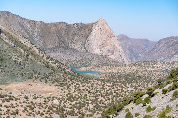 The beautiful mountain trekking road with clear blue sky and rocky hills and fresh mountain lake in Fann mountains in Tajikistan