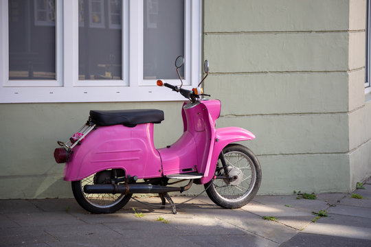 Pinkfarbenes Moped / Schwalbe vor einer Hausfassade