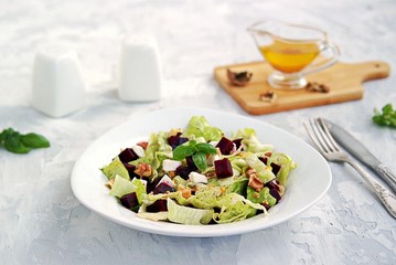 Green salad with boiled beetroot, feta and walnuts in a white plate on a gray concrete background. Seasoned with olive oil, grain mustard and vinegar. Healthy food.