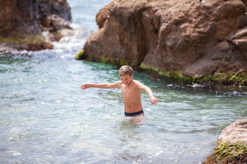 Fototapeta premium Happy beautiful teenager is swimming in the sea, a boy comes out of the water