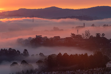 Obraz premium Mountains in fog at beautiful morning in autumn in Dalat city, Vietnam. Landscape with Langbiang mountain valley, low clouds, forest, colorful sky , city illumination at dusk.