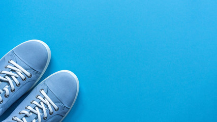 Light blue sneakers with white laces and a white sole on a blue flat lay background. Copy space. Lifestyle, outdoor shoes for walking. Casual unisex