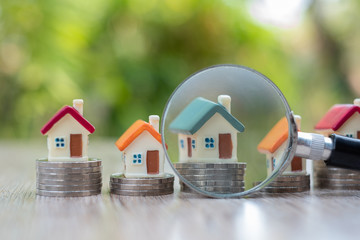A magnifying glass placed near the house model placed on a pile of coins Search for houses, investment ideas, real estate, buy and sell houses, house selection, rental taxes, search