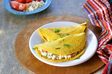 Chilla, tortillas or pancakes made from chickpea flour stuffed with cheese panir and tomato on a white plate on a gray concrete background. Indian food, street food. Vegetarian recipes.