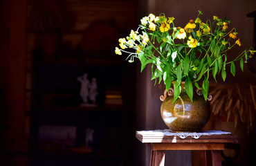 Bouquet of yellow wildflowers gelenium, echinacea in a conic ceramic vase on a small wooden table.