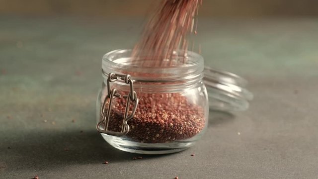 Red raw quinoa, South American grain, fall in glass jar. Healthy and gluten free food.
