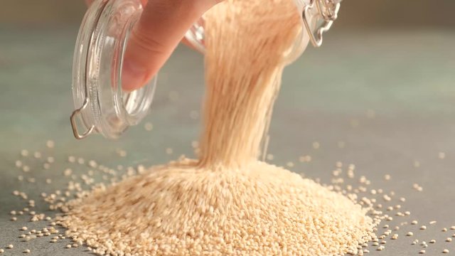 White raw quinoa, South American grain, female hands open glass jar and sprinkle seeds. Healthy and gluten free food.