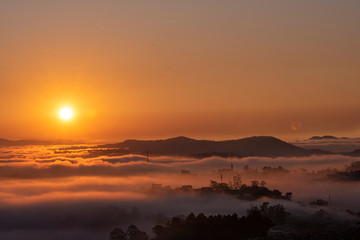 Mountains in fog at beautiful morning in autumn in Dalat city, Vietnam. Landscape with Langbiang mountain valley, low clouds, forest, colorful sky , city illumination at dusk.