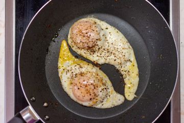 Two fried eggs in a pan fried in oil on a black pan. They look like yin and yang.