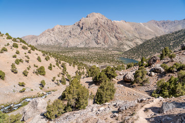 The beautiful mountain trekking road with clear blue sky and rocky hills and fresh mountain stream in Fann mountains in Tajikistan