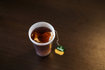 disposable plastic cup with tea bag on the table. ecology problems. quick snack at work. office