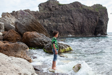 Happy hamdsome teen walks along the sea coast against the background of the sea, from behind a beautiful landscape