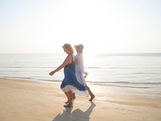 Two funny older women walking and laughing at sea shore at sunny day