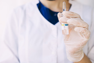 young woman doctor in white coat and blue surgeon suit holds in her hand a bottle with a medicine, vaccine. Coronavirus pandemic.