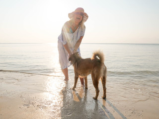 Funny senior woman playing wih dog at seashore in sunlight
