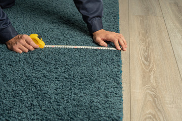 A store employee measures the length of a carpet for a customer