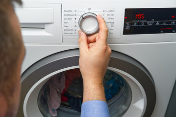 The man sets the program and turns on the washing machine. Close-up Of Person Hand Pressing Button...