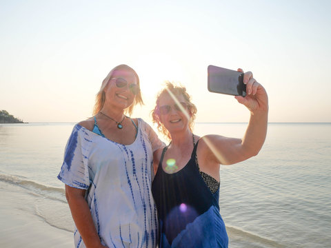 Happy senior women making selfie on smartphone at sunset beach