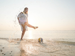Senior woman playing with a ball splashing water in sun glare