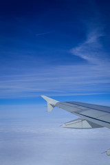 View over the clouds from the porthole of an airplane with plane wing and blue sky