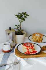 Pancakes near coffee maker on white table in kitchen. Morning breakfast at home in quarantine. Recipe of homemade delicious pancakes.