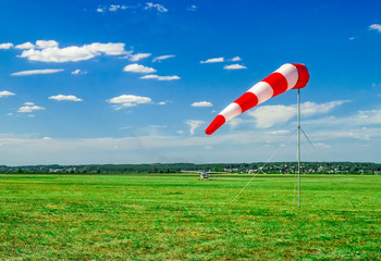 Red and white windsock wind sock on blue sky, green field and clouds background on aerodrome or...