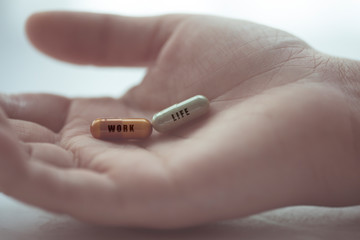 Closeup hand of the person holding the pill or drug capsule that stamp the word Work and Life. Decision to choose between work or life. Work Life Balance concepts.