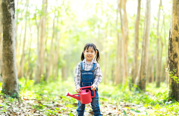 Kids gardener holding water can in hands, helping her family to water the plant in summer during school close. Outdoor family activity to work as a planter with a smiling face, fun, and enjoyable.